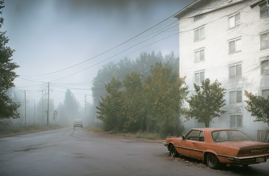 Abandoned rusty car on foggy day with white building and trees