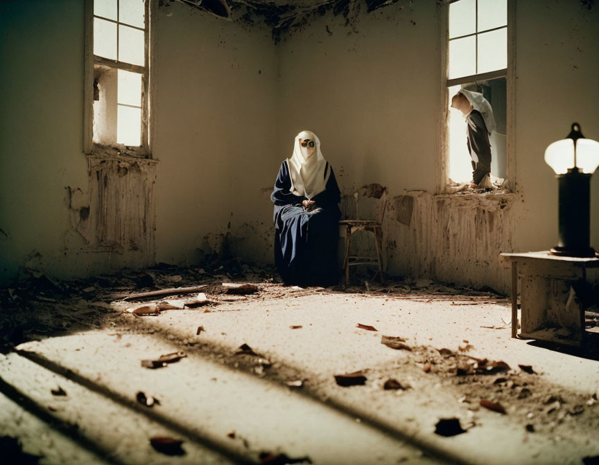 Person in hijab sits in dilapidated room with sunlight, debris, and lit lamp
