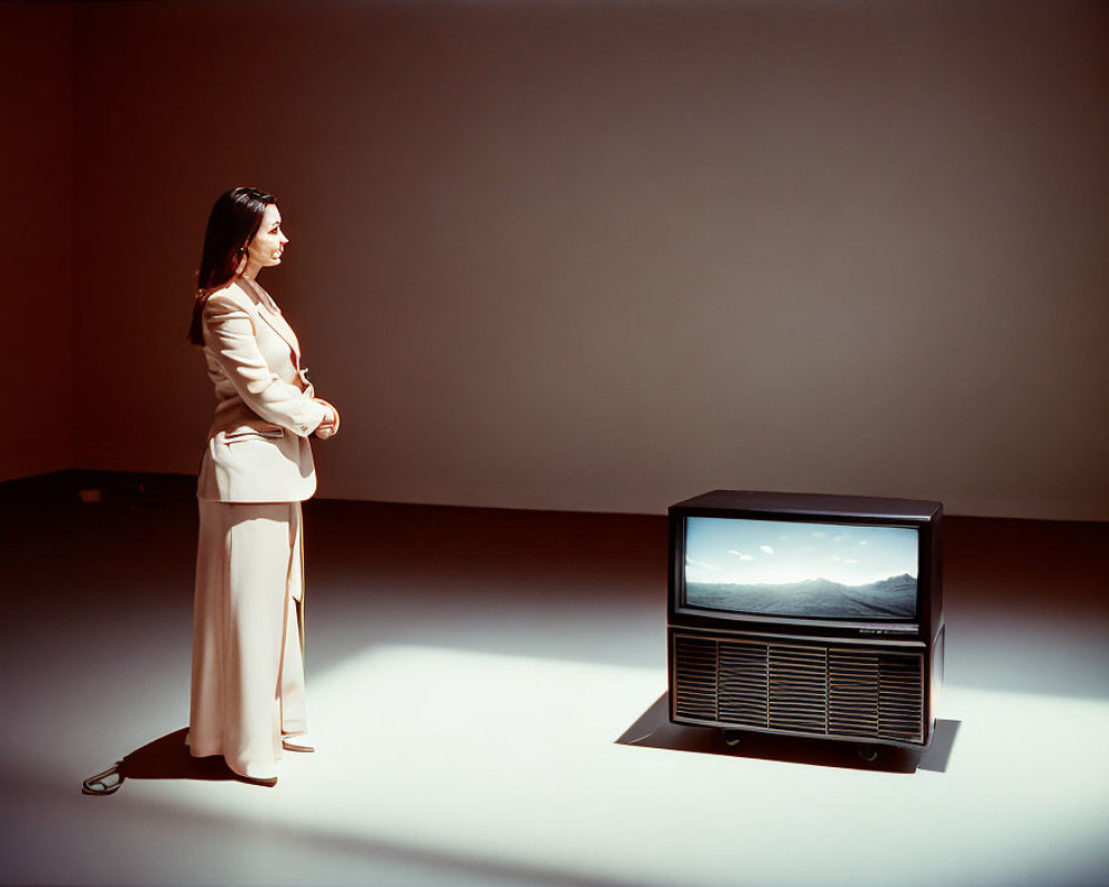Woman in beige suit gazes at mountain scene on old TV