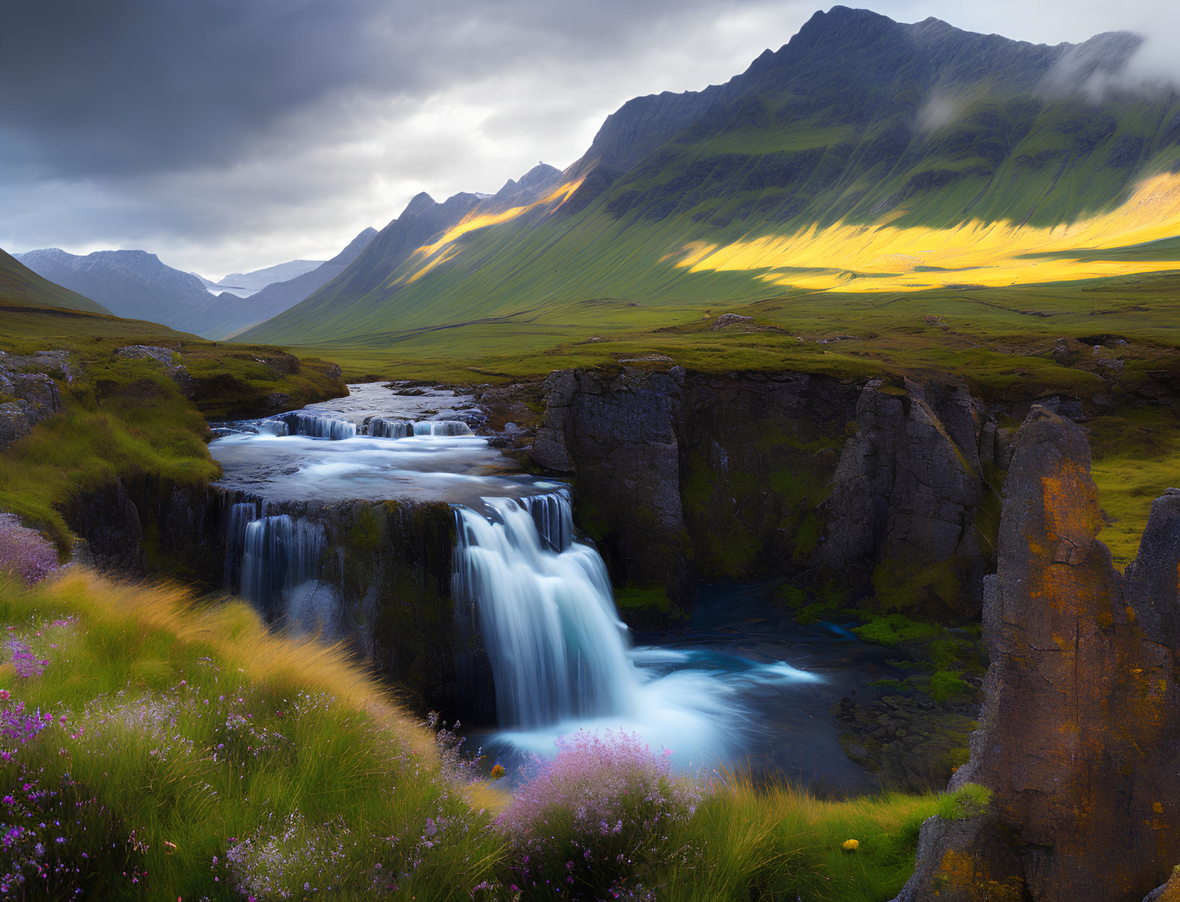 Scenic waterfall in lush landscape with wildflowers and mountains