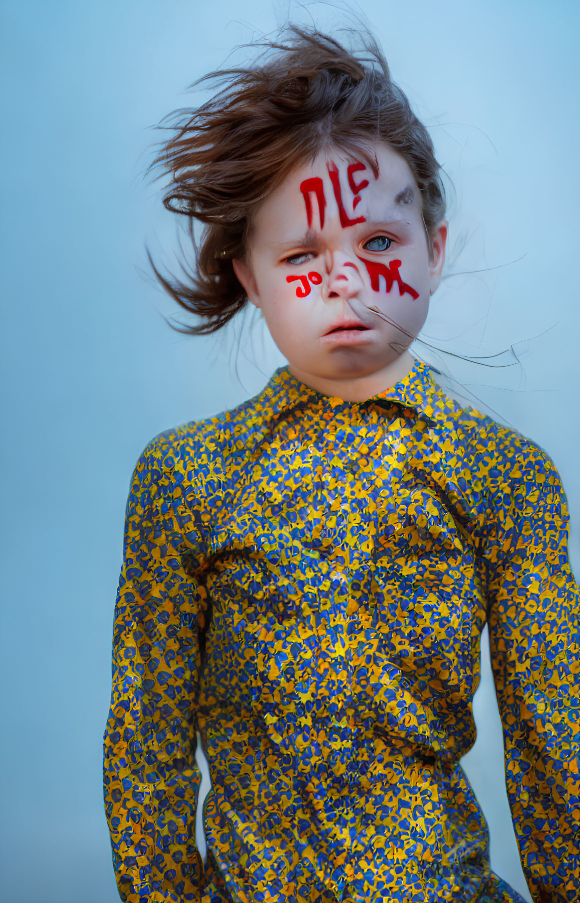 Child with solemn expression in yellow shirt with red writing on face