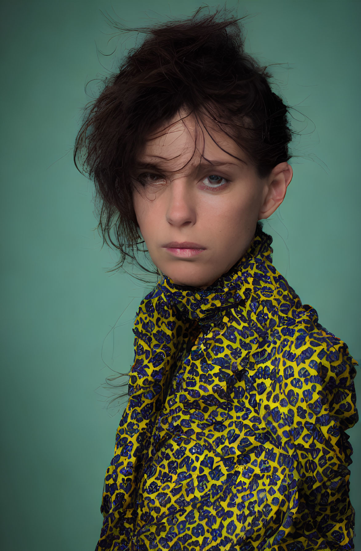 Tousled hair person in yellow and black top against teal background