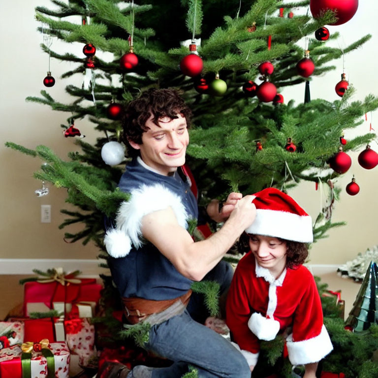 Man and child in Santa hats decorate Christmas tree with presents