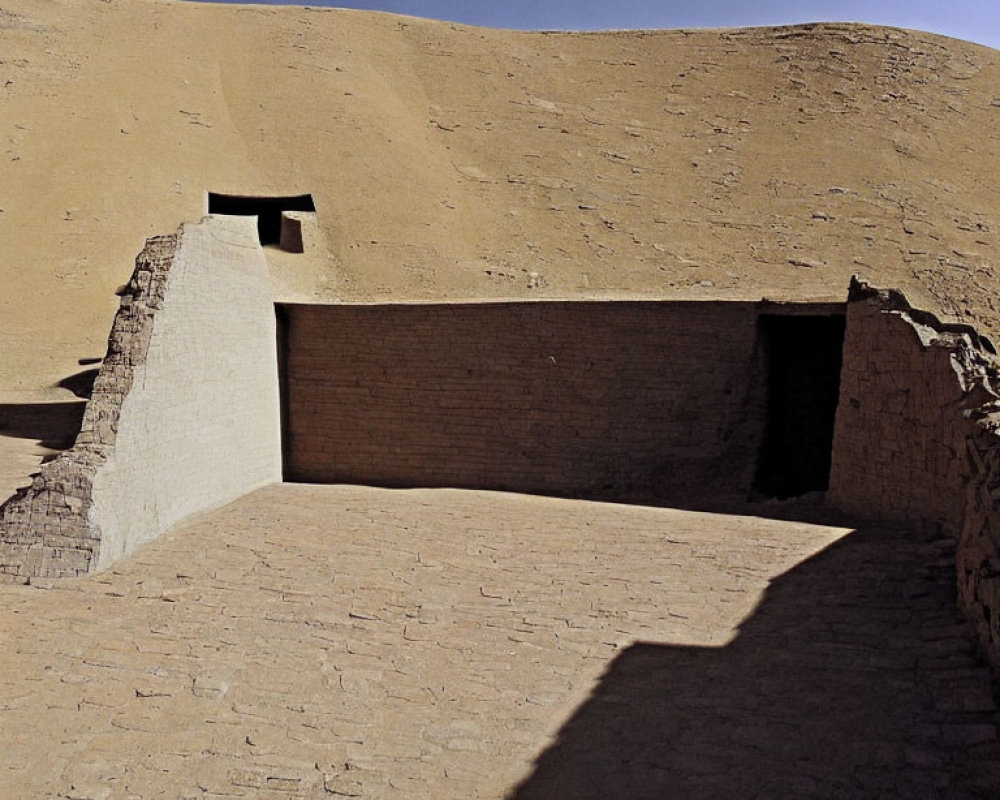 Ancient adobe ruins in desert with small rectangular opening and contrasting shadows