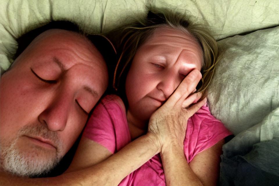 Two individuals lying in bed with eyes closed, one displaying distress or fatigue.
