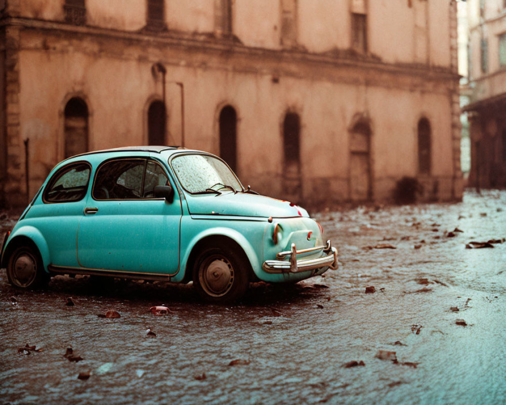 Vintage blue car on wet street near old buildings with fallen leaves, evoking a rainy day ambiance