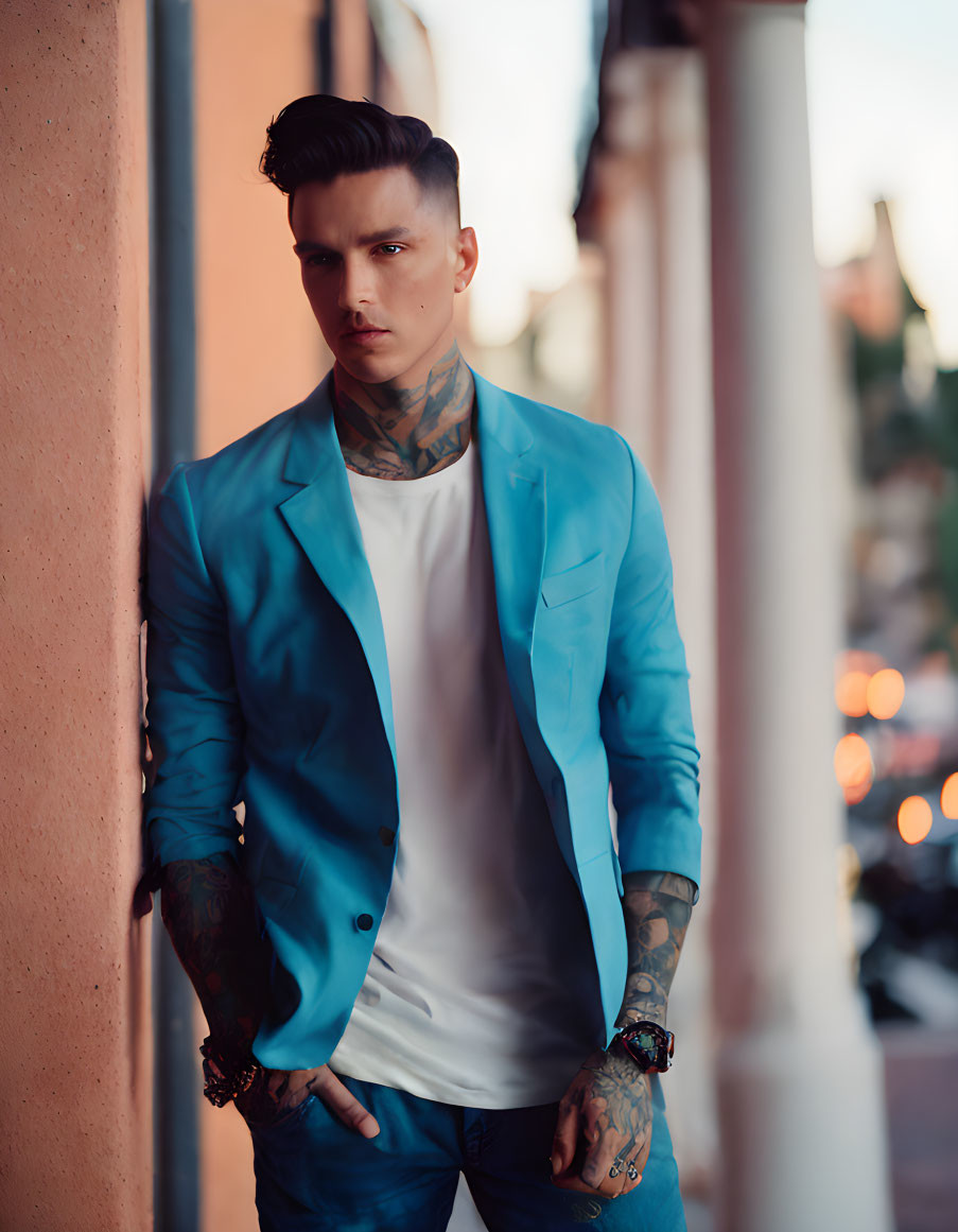 Tattooed man in blue blazer leaning against wall