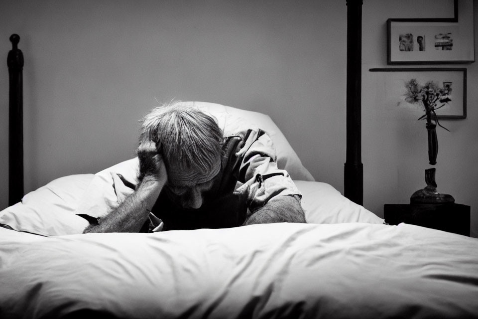 Elderly person in distress on bed in black and white