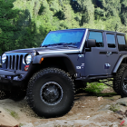 Modified Jeep Wrangler in misty forest with off-road tires, extra lights, and roof gear