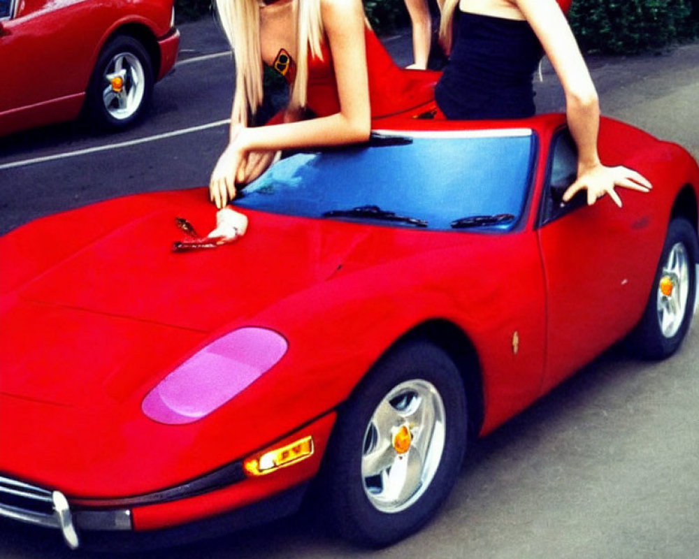 Two women posing with a red Ferrari in front of trees.