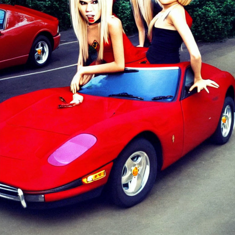 Two women posing with a red Ferrari in front of trees.