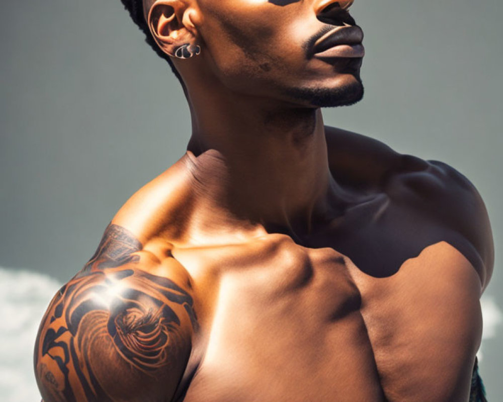 Muscular shirtless man with arm tattoo in pensive pose on soft backdrop