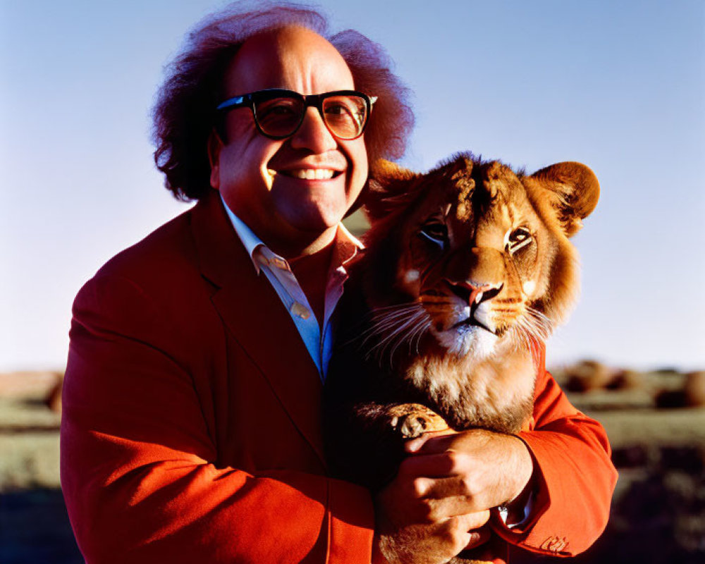 Man in large glasses holds lion cub in sunny outdoor scene