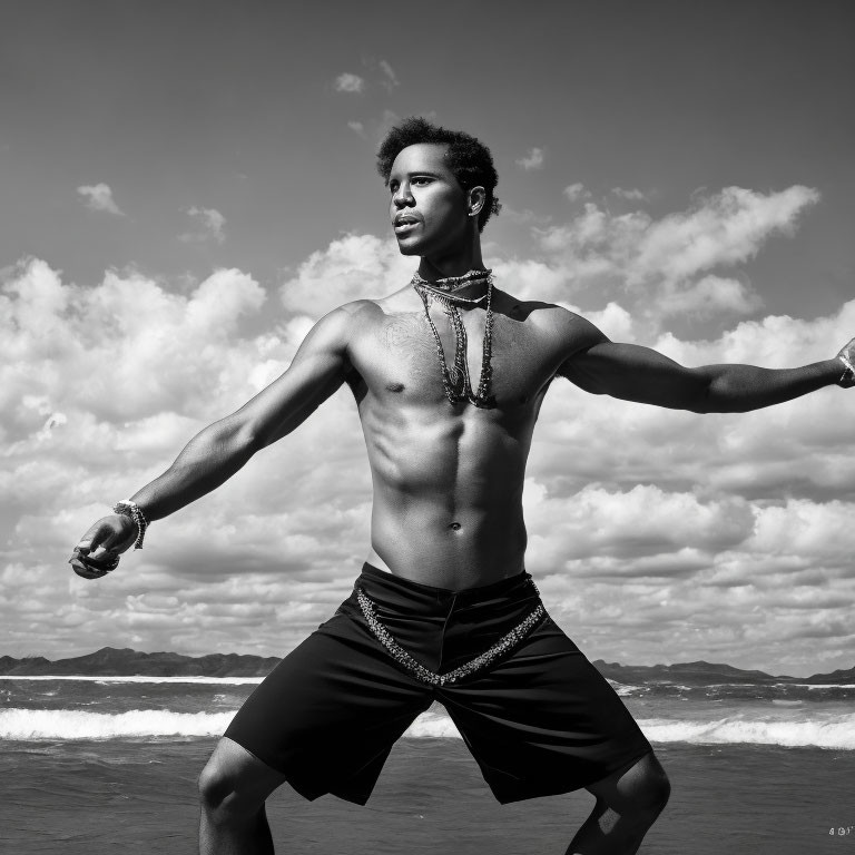 Toned shirtless man on beach with outstretched arms