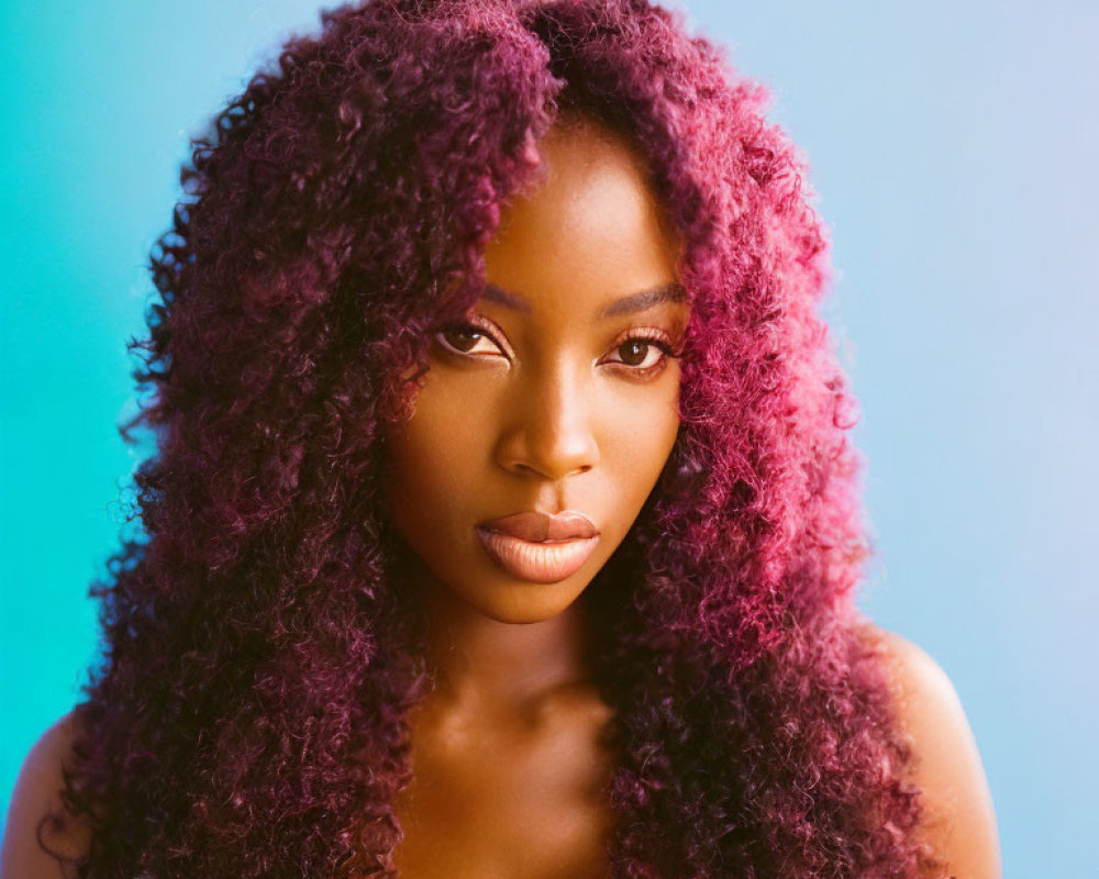 Portrait of woman with curly magenta hair against blue backdrop
