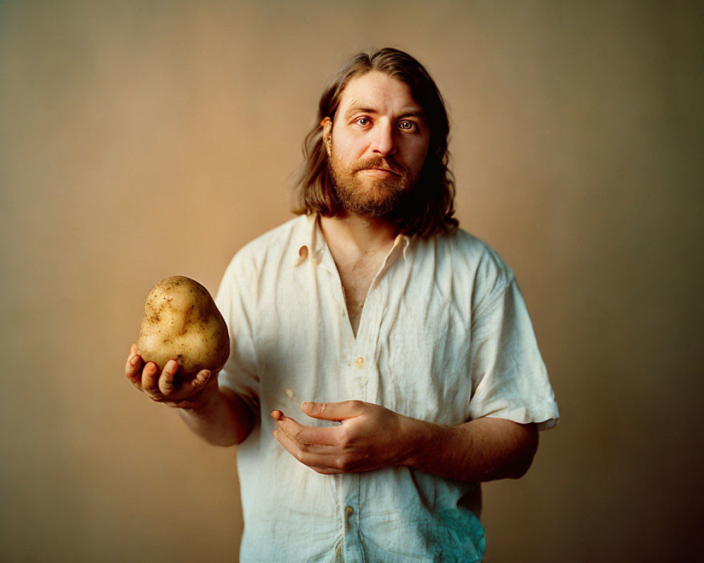 Man with medium-length hair and beard holding a potato on plain background