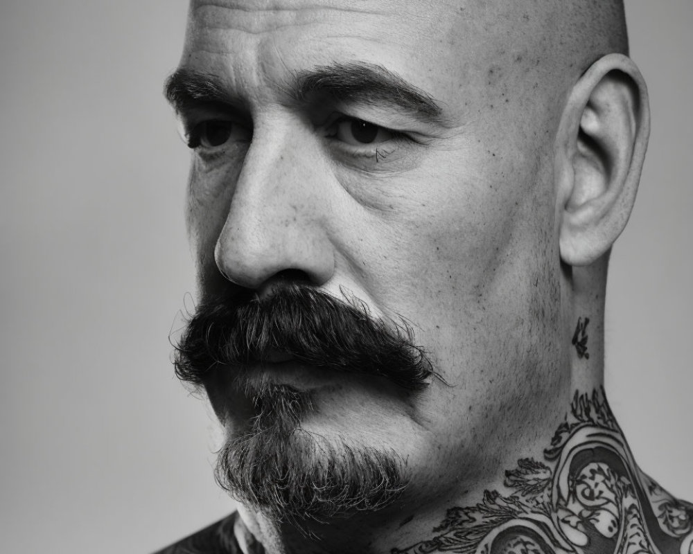 Bald Man with Thick Mustache and Neck Tattoos on Gray Background