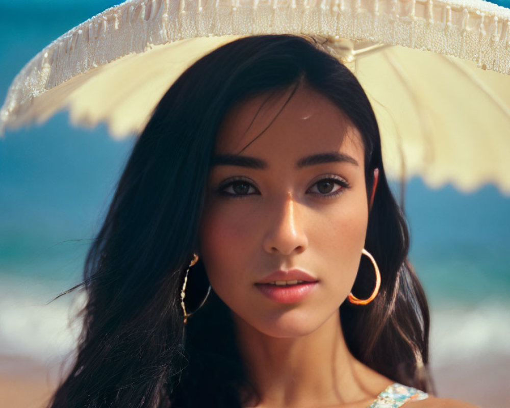 Dark-haired woman with hoop earrings holding a white parasol on a beach
