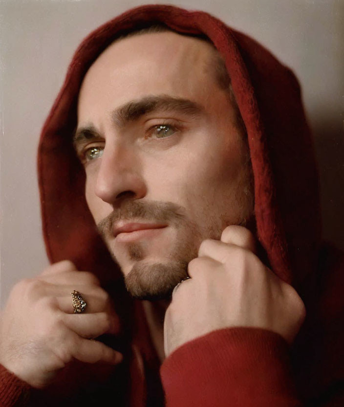 Bearded man in red hooded garment gazes thoughtfully aside