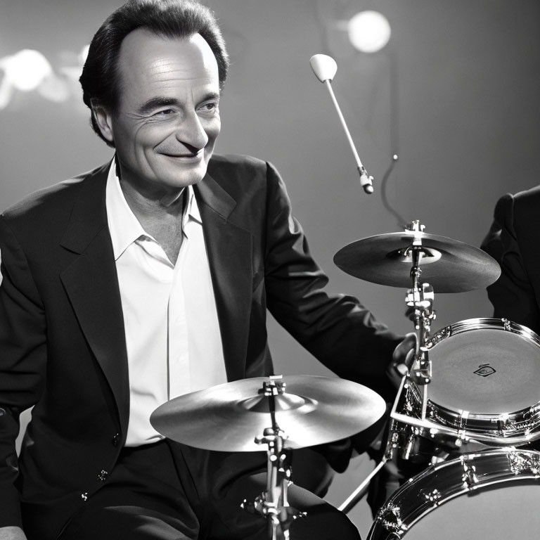 Monochrome image of man in suit smiling behind drum set