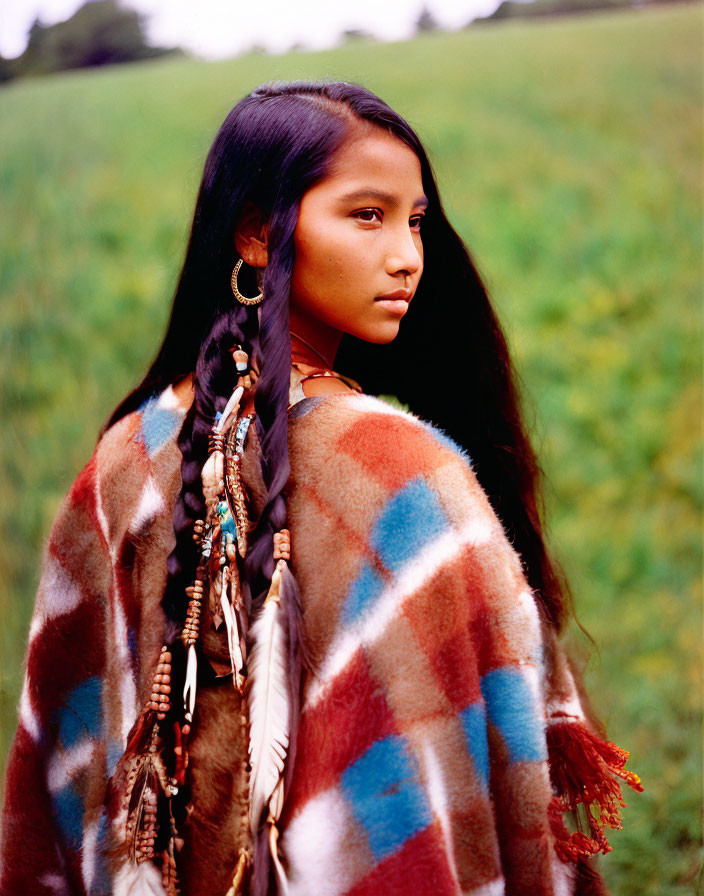 Young woman with dark hair and feathered adornments in colorful shawl on green field
