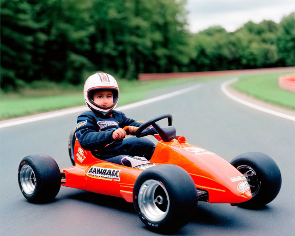 Child in racing suit and helmet drives orange go-kart on outdoor track