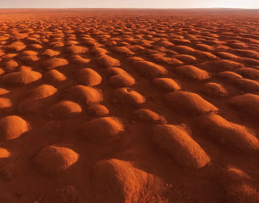 Vast desert landscape with rounded reddish mounds under orange sky