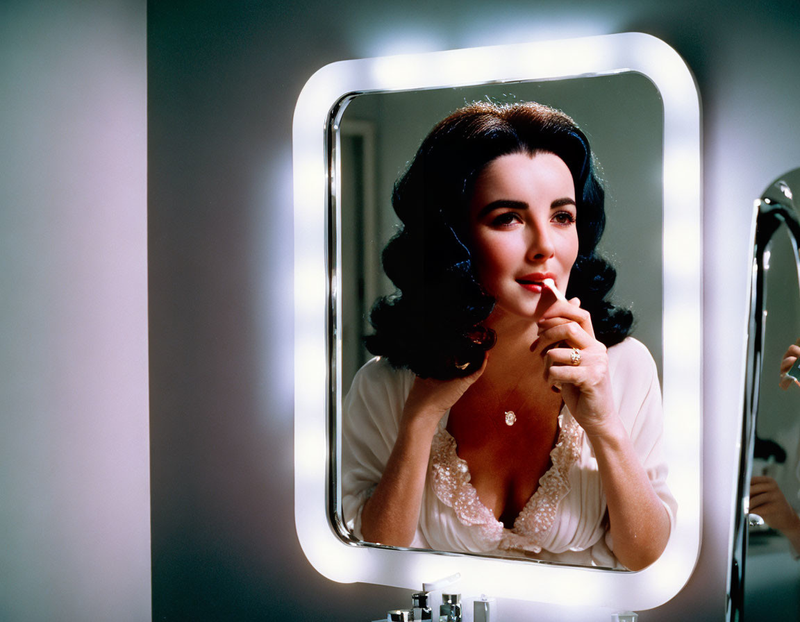 Dark-haired woman applies lipstick in front of bright lights mirror
