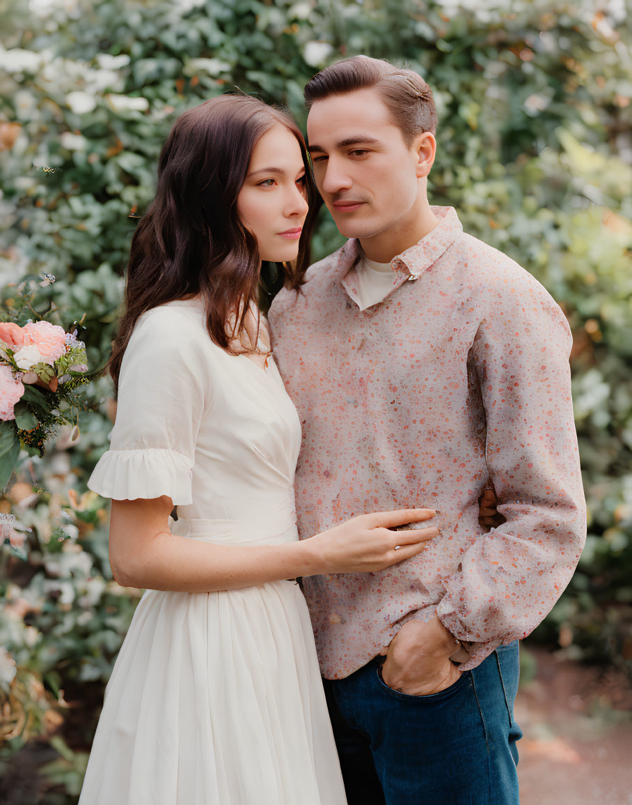 Couple in White Dress and Patterned Shirt Surrounded by Green Foliage and Pink Flowers