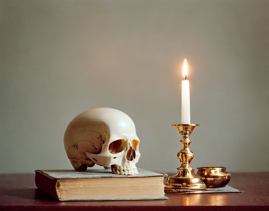 Skull on old book with lit candle in brass holder