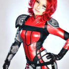 Red-haired person with blue eyes in red and silver latex suit with black gloves exudes futuristic superhero vibe