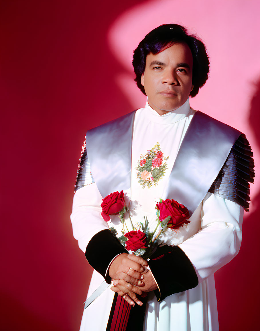 Person in White Suit with Floral Design Holding Red Roses on Red Backdrop