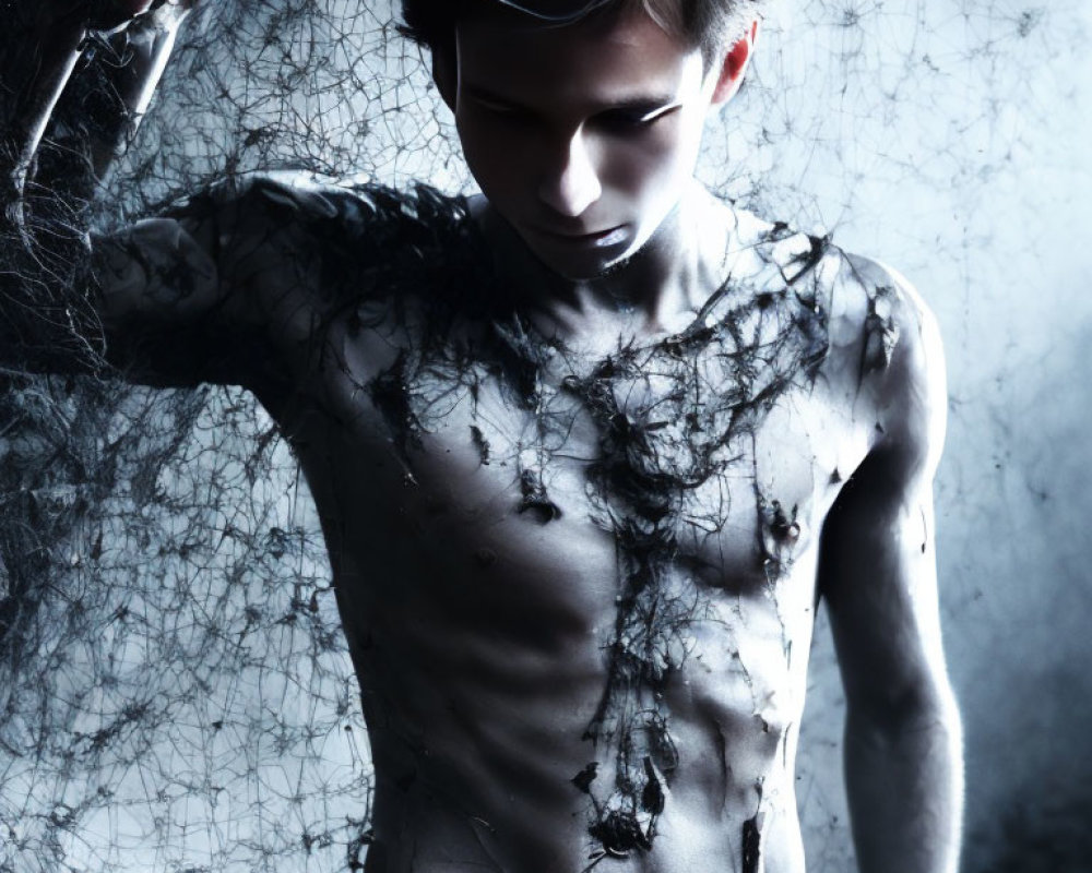Dark-haired shirtless man covered in cobwebs in haunting setting