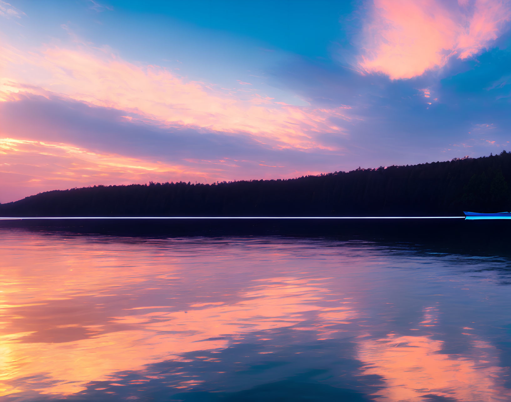 Colorful sunset over calm lake with forested horizon