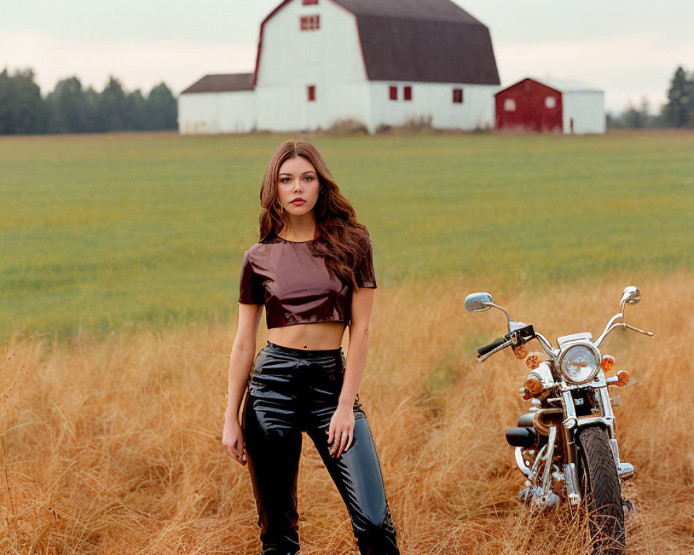 Woman in crop top and black pants by motorcycle in field with barn