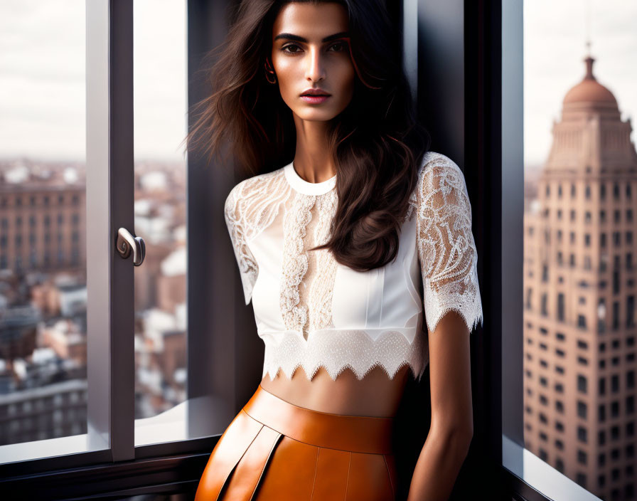 Stylish woman in white lace top and orange leather skirt by open window