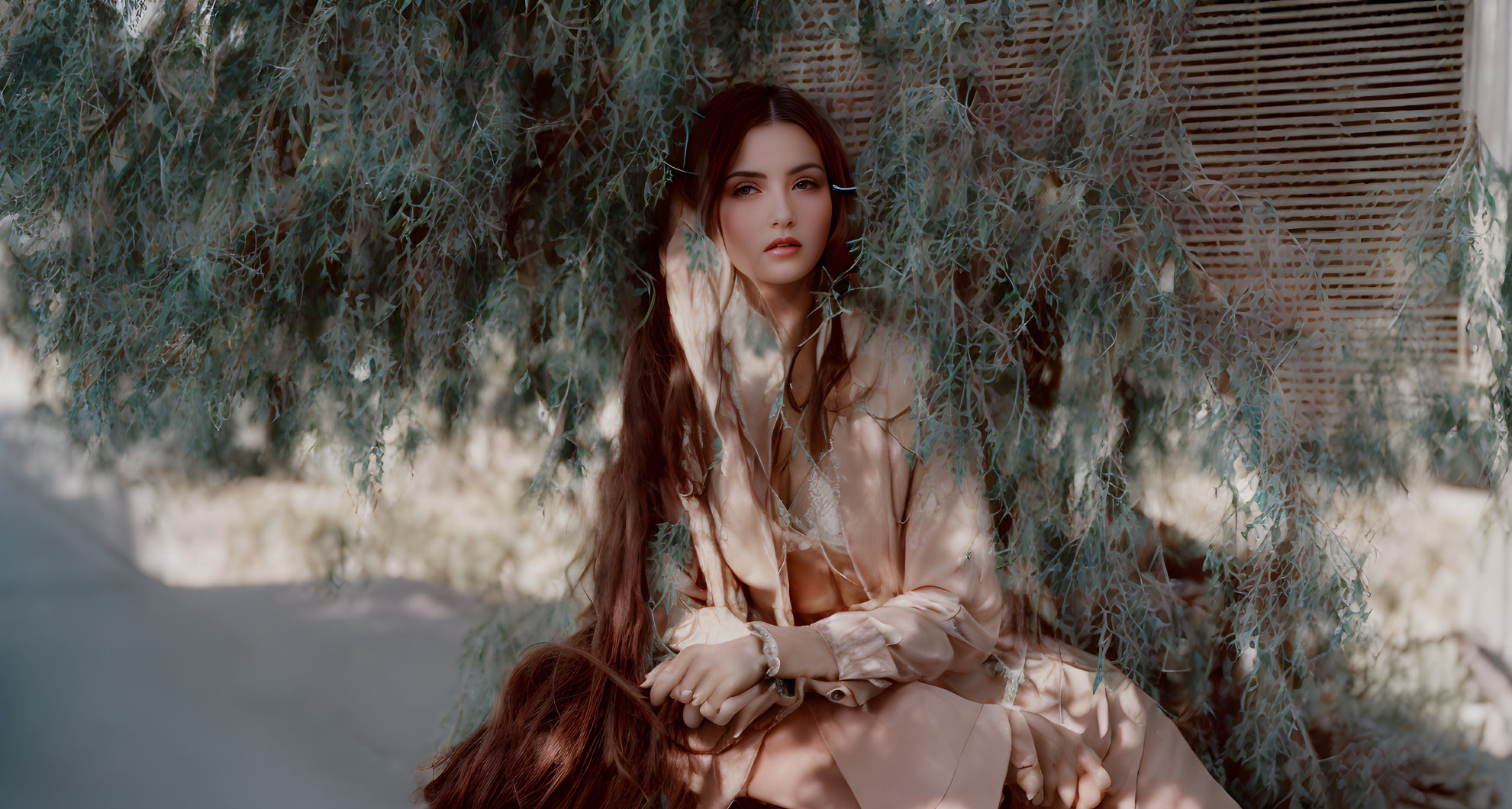 Long-haired woman in beige outfit sitting under tree with wispy foliage