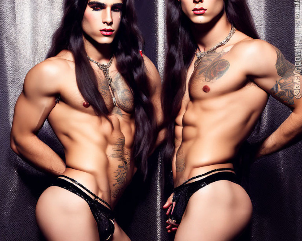 Long-haired twin models in black underwear pose with tattoos on metallic backdrop