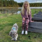 Young girl in pink jacket with white dogs by lake
