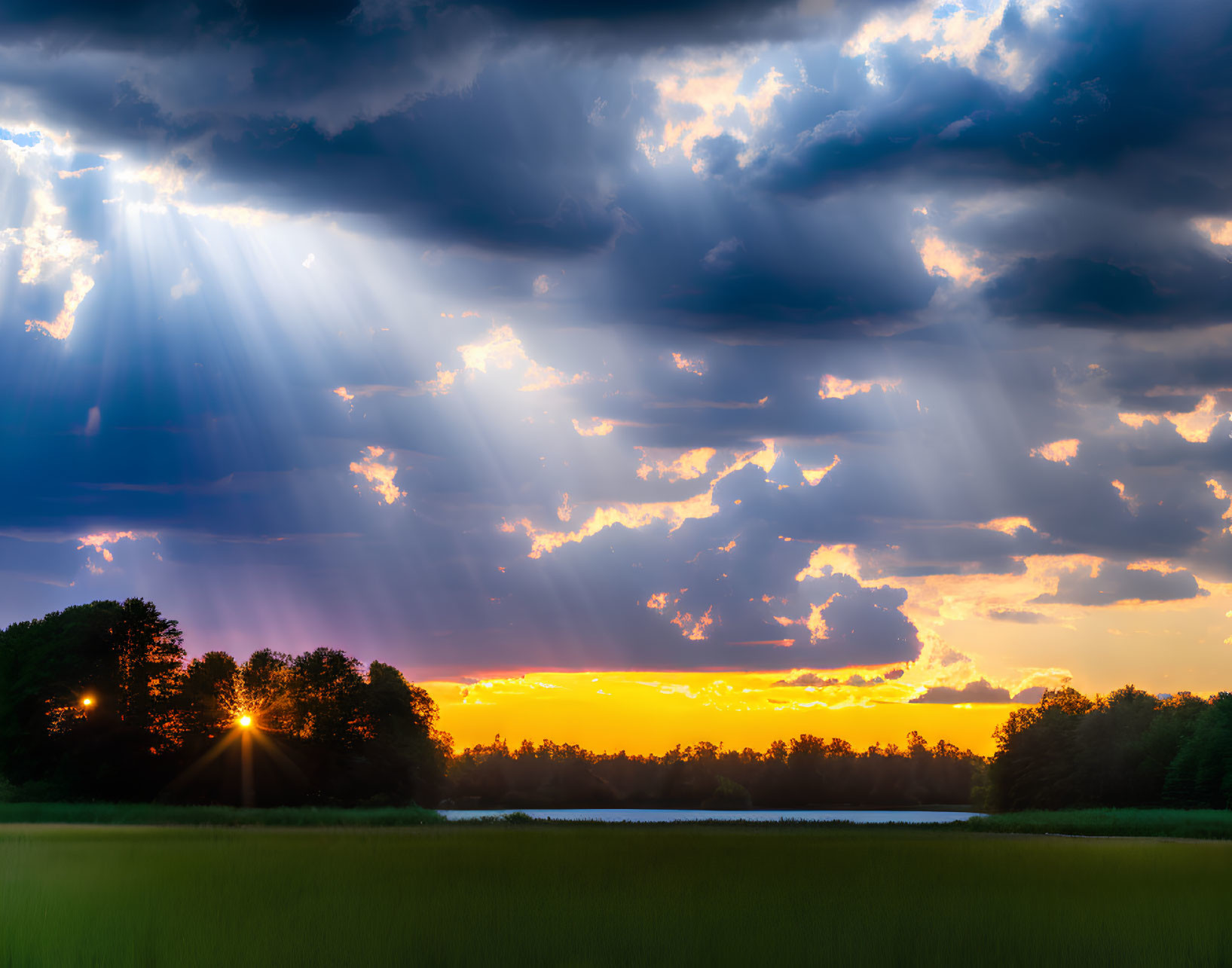 Dramatic sunset scene over field with sunbeams and water reflections