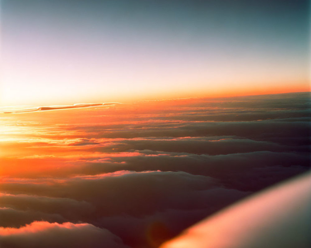 Sunset view above clouds with warm orange hues and wingtip visible