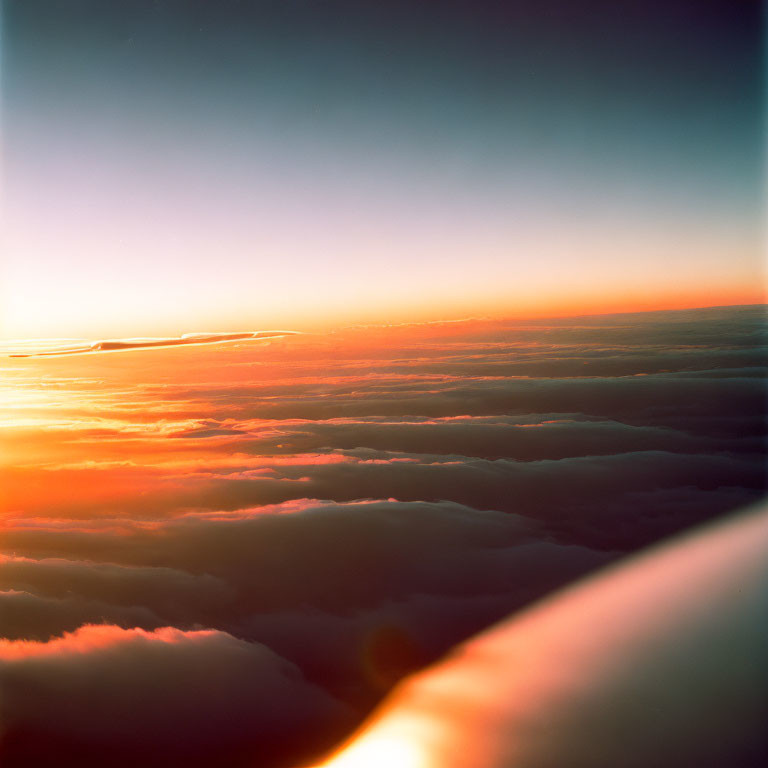 Sunset view above clouds with warm orange hues and wingtip visible