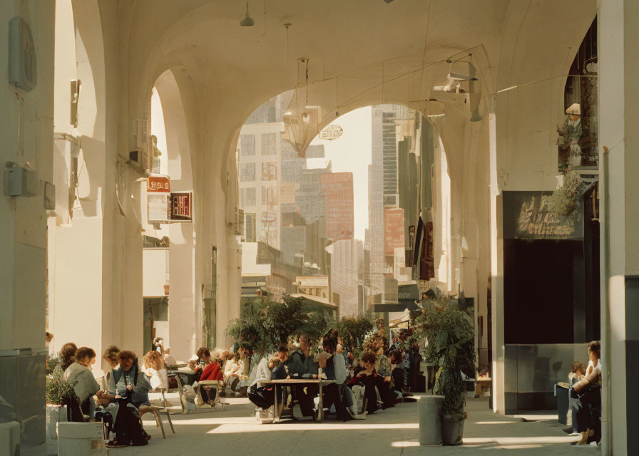 Urban arcade with people at tables, architectural arches, cityscape in background
