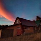 Cozy wooden house under starry night sky with crescent moon and vibrant nebula colors