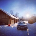 Mercedes car parked near snowy wooden cabins at sunset