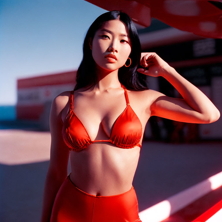 Woman in Orange Bikini Poses Against Blue Sky and Red Structure