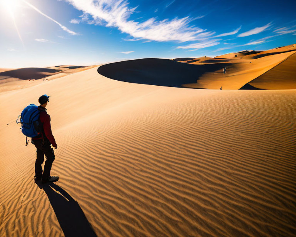 Traveler with Blue Backpack Standing on Desert Dune Under Clear Sky