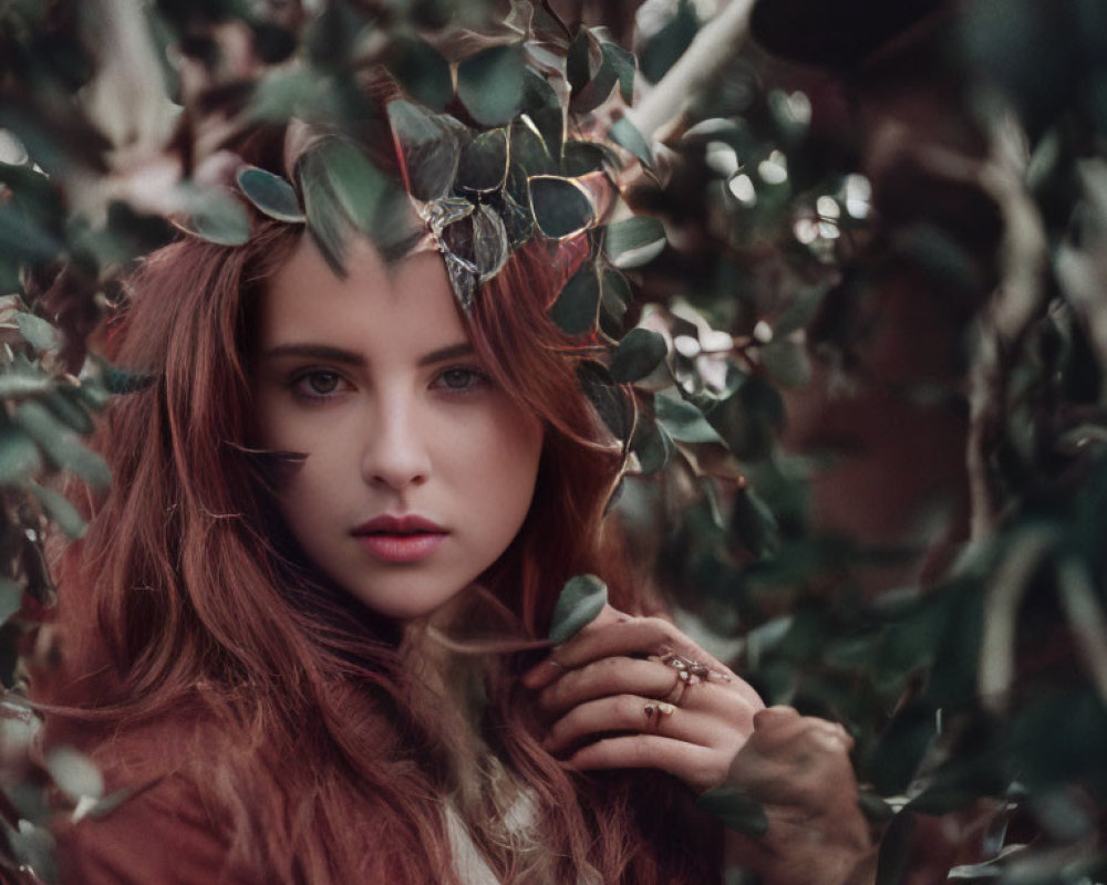 Red-haired woman gazes through green leaves in soft-focus forest ambiance