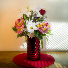 Colorful bouquet with lilies and orange flowers in red vase, green apple, and fabric on reflective