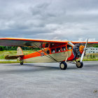 Vintage orange and white biplane with radial engine on tarmac under cloudy sky